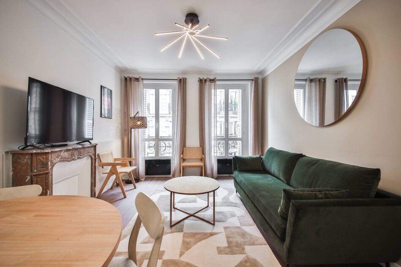 Una sala de estar con un sofá verde, una mesa de comedor de madera y un televisor sobre un mueble de mármol.
