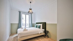 Ein Schlafzimmer mit Bett, einer Hängeleuchte, einem Fenster mit Vorhängen und einem Balkon.
