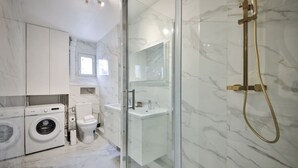 Ein modernes Badezimmer mit Duschkabine aus Glas, einer Waschmaschine und einer Toilette.