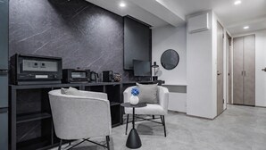 A modern kitchen with a dark marble backsplash, a built-in microwave, and a coffee machine. There are two grey armchairs and a small table with a vase and flowers.