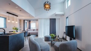 A modern living space with a kitchen island, grey upholstered seating, a dining area, and a flat-screen TV.