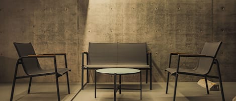 A room with a sofa and two chairs, a small round table, and a concrete wall.