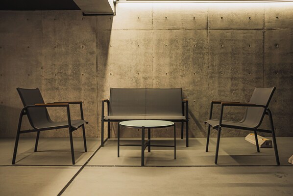 A room with a sofa and two chairs, a small round table, and a concrete wall. - SLL Urban Suites Ebisu (Shibuya-ku)