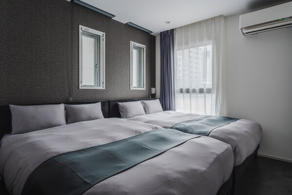A hotel room with two beds, a dark textured wall, a window with curtains, and an air conditioning unit.