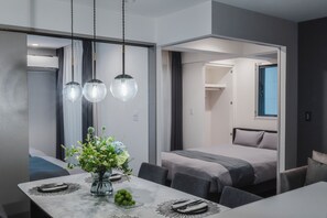 Habitació d'hotel moderna amb zona de menjador, llit i bany visible a través d'una porta oberta.