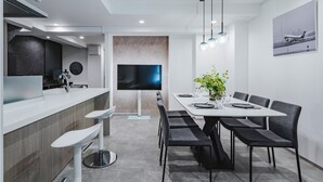 Un espace repas moderne avec une longue table, de nombreuses chaises, un comptoir de bar et un grand téléviseur à écran plat.