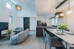 Una cocina moderna con una isla central, una zona de comedor con una mesa larga y sillas, y un espacio de estar con un sofá y una pequeña mesa.
