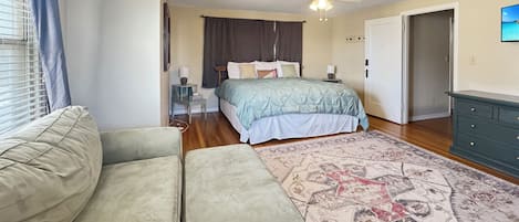 Ein Schlafzimmer mit Bett, Deckenventilator, Nachttisch, Kommode und einem gemusterten Teppich.