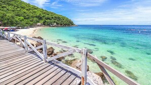 Un muelle de madera que lleva a una playa con agua turquesa cristalina y una colina boscosa al fondo.