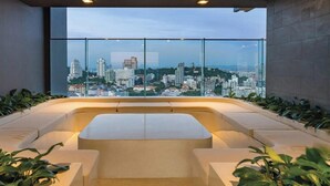 Un moderno salón con vista a la ciudad, que incluye una zona de estar con asientos curvos y plantas en macetas.