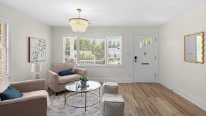 A room with a chandelier, a round coffee table, a beige sofa, a patterned rug, and a door with a mirror.