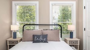 A bed with a headboard, two bedside tables, and a window with blinds.