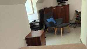 Quarto com cama, escrivaninha, cadeira e televisão.