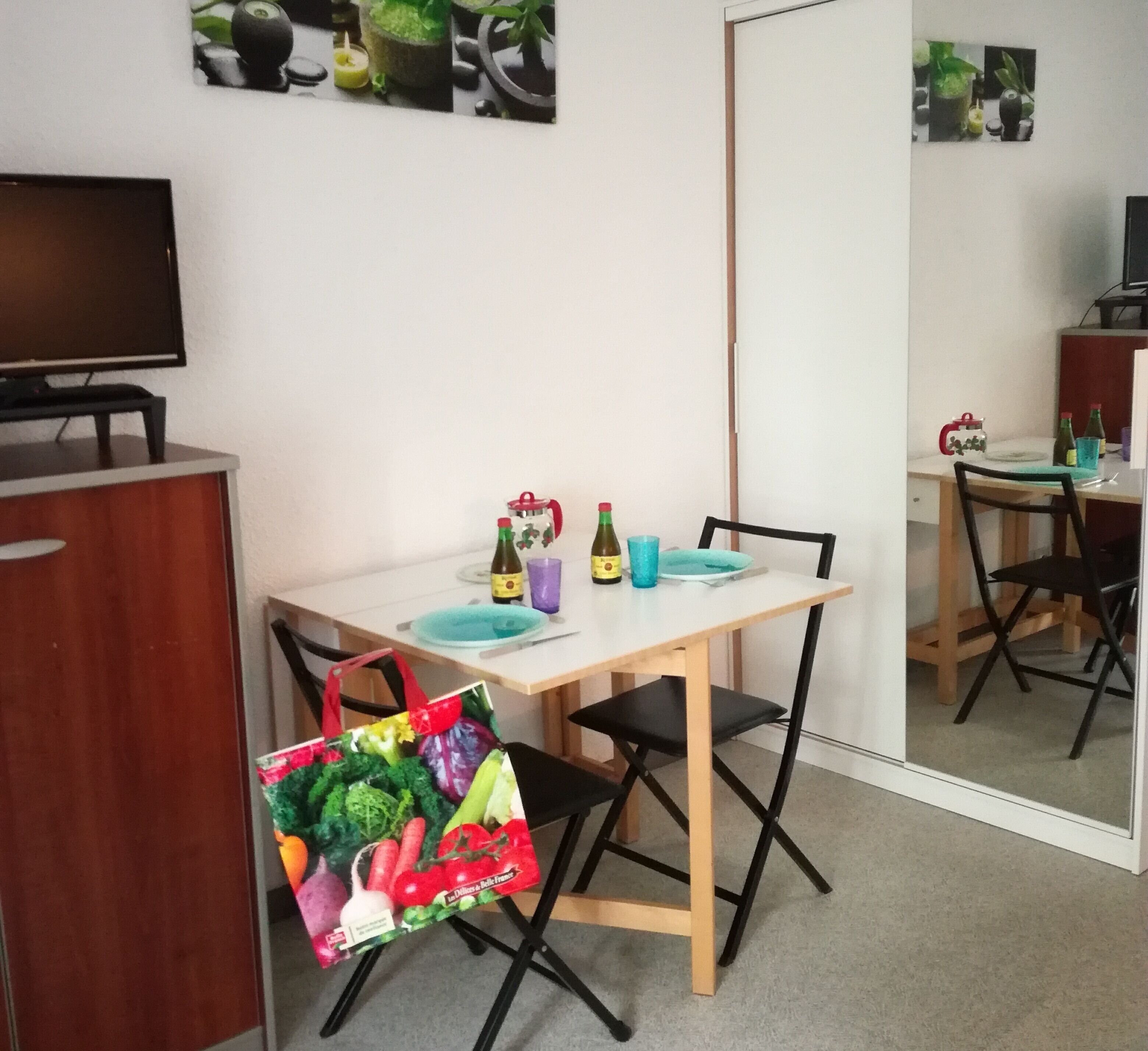 A dining area with a table, chairs, a television, and a mirror.