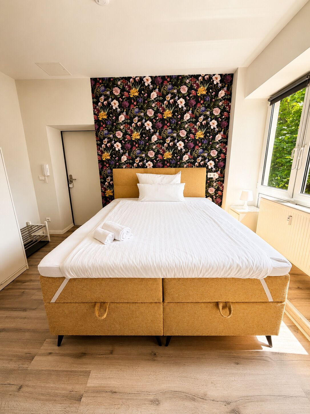 A bedroom with a bed, a floral wallpaper, a window, and a door.