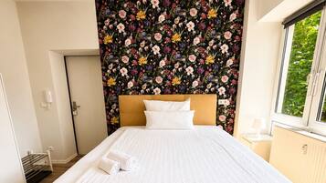 A bedroom with a bed, a floral wallpaper, a window, and a door.