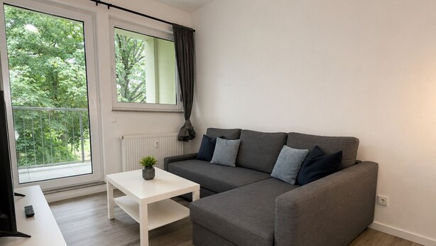 A modern living room with a grey sofa, white coffee table, and a view of greenery through large windows. - MIILOX Apartments Chemnitz Rosenhof (Chemnitz)