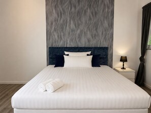 A neatly made bed with pillows and rolled towels, a bedside lamp, and a wall with a textured pattern.