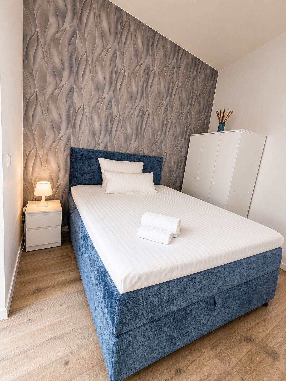 Une chambre à coucher comprenant un lit, une table de chevet, une lampe et une armoire.
