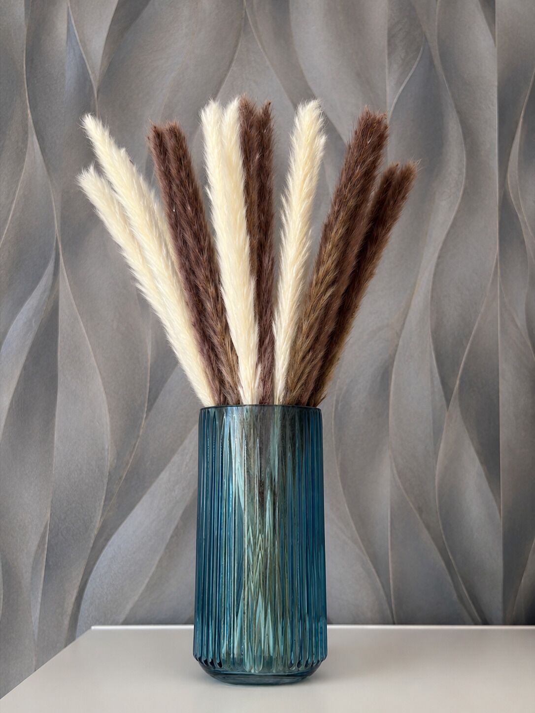 A glass vase with a ribbed texture filled with feather-like objects.