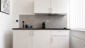 A kitchen with white cabinets, a black countertop, and a window with blinds. - MIILOX Apartments Chemnitz Rosenhof (Chemnitz)