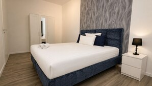 A modern bedroom with a large bed, a nightstand, a mirror, and a textured wall. - MIILOX Apartments Chemnitz Rosenhof (Chemnitz)