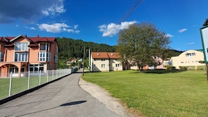 Una calle pavimentada que conduce a una zona residencial con casas, un campo cubierto de césped y un árbol.