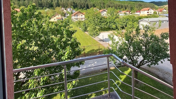 Un balcón con vistas a una zona residencial, una colina boscosa y un cielo despejado.