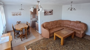 Una sala de estar con sofá, una mesa de comedor con sillas, un tapete y una zona de cocina al fondo.