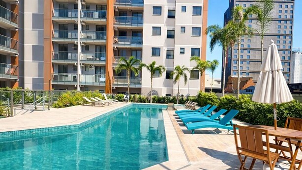 Una piscina con sillas de descanso y una palmera, rodeada por un edificio de gran altura.