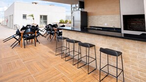 Un patio exterior con una mesa larga y sillas, un muro de ladrillo y una cocina moderna.