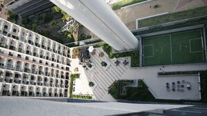 Un edificio de gran altura con terraza en la azotea, campo deportivo y diseño arquitectónico moderno.