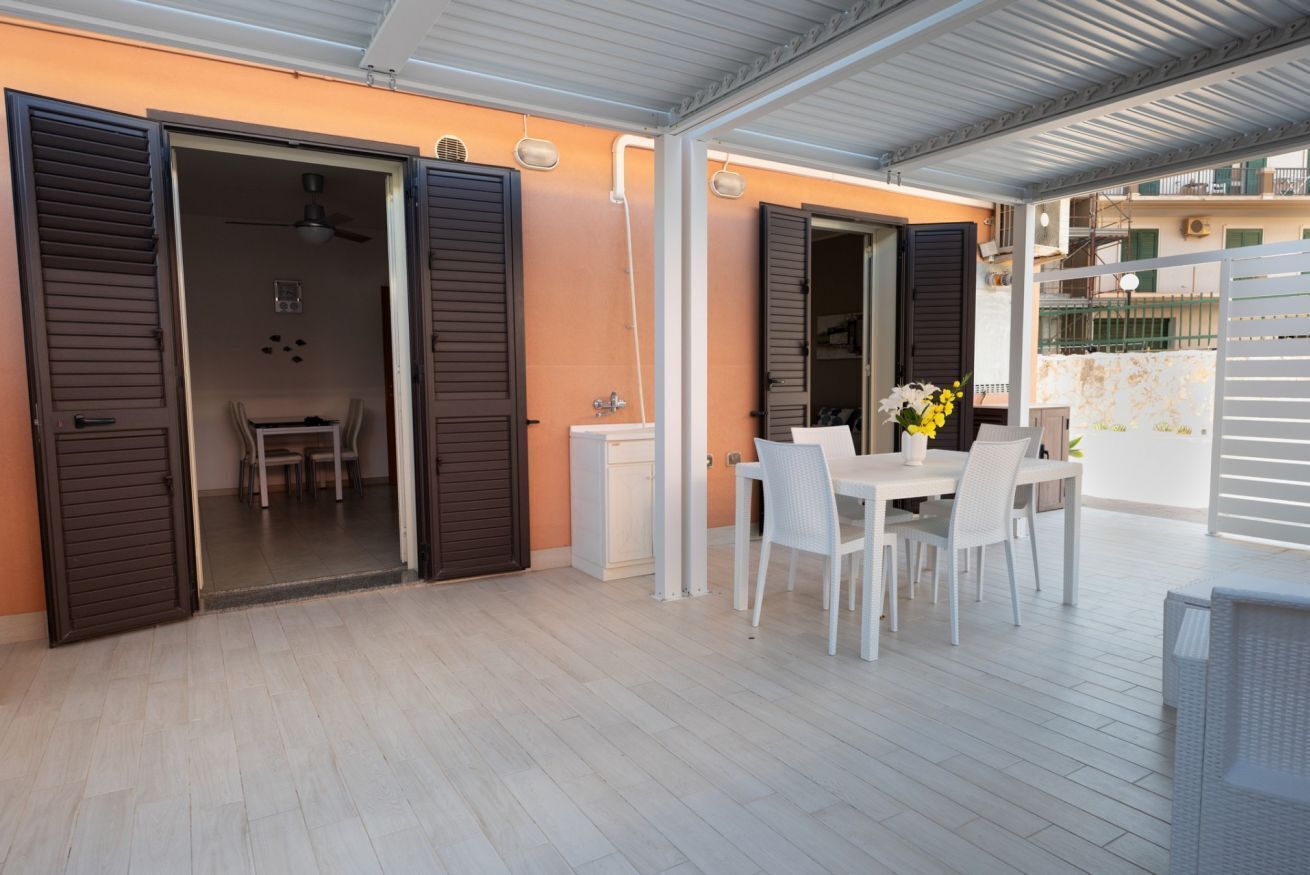 Un patio esterno con tavolo e sedie, una ventola a soffitto e vista sugli edifici circostanti.
