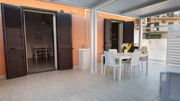 Un patio esterno con tavolo e sedie, una ventola a soffitto e vista sugli edifici circostanti.