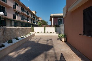 A courtyard with a stone pathway, potted plants, and a building with balconies. - Cozy 55 sqm apartment that can accommodate up to 4 guests, located on the ground floor of a building (accessible via a few steps). The property is situated in Pozzallo—a seaside town with beaches that have repeatedly been awarded the Blue Flag—in a q (Pozzallo)