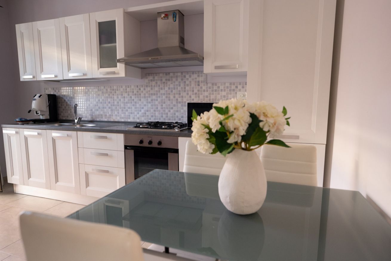 A modern kitchen with white cabinets, a glass table, and a vase of flowers.