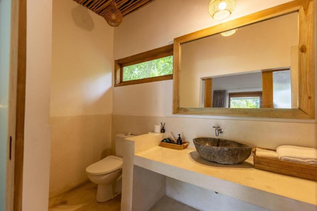 Baño con inodoro, lavabo de piedra, espejo y ventana.