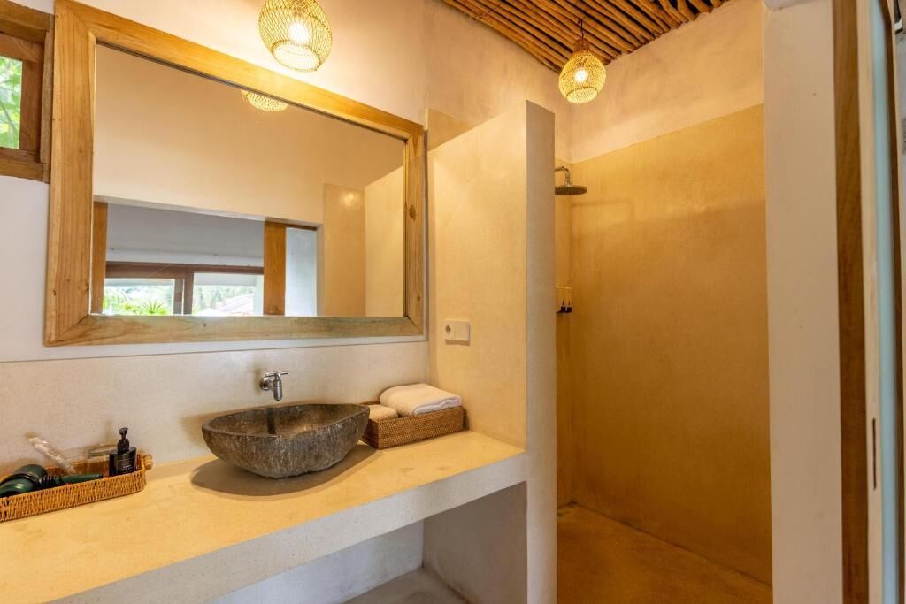 Een badkamer met een stenen wasbak, een spiegel met houten lijst en een douchehoek.