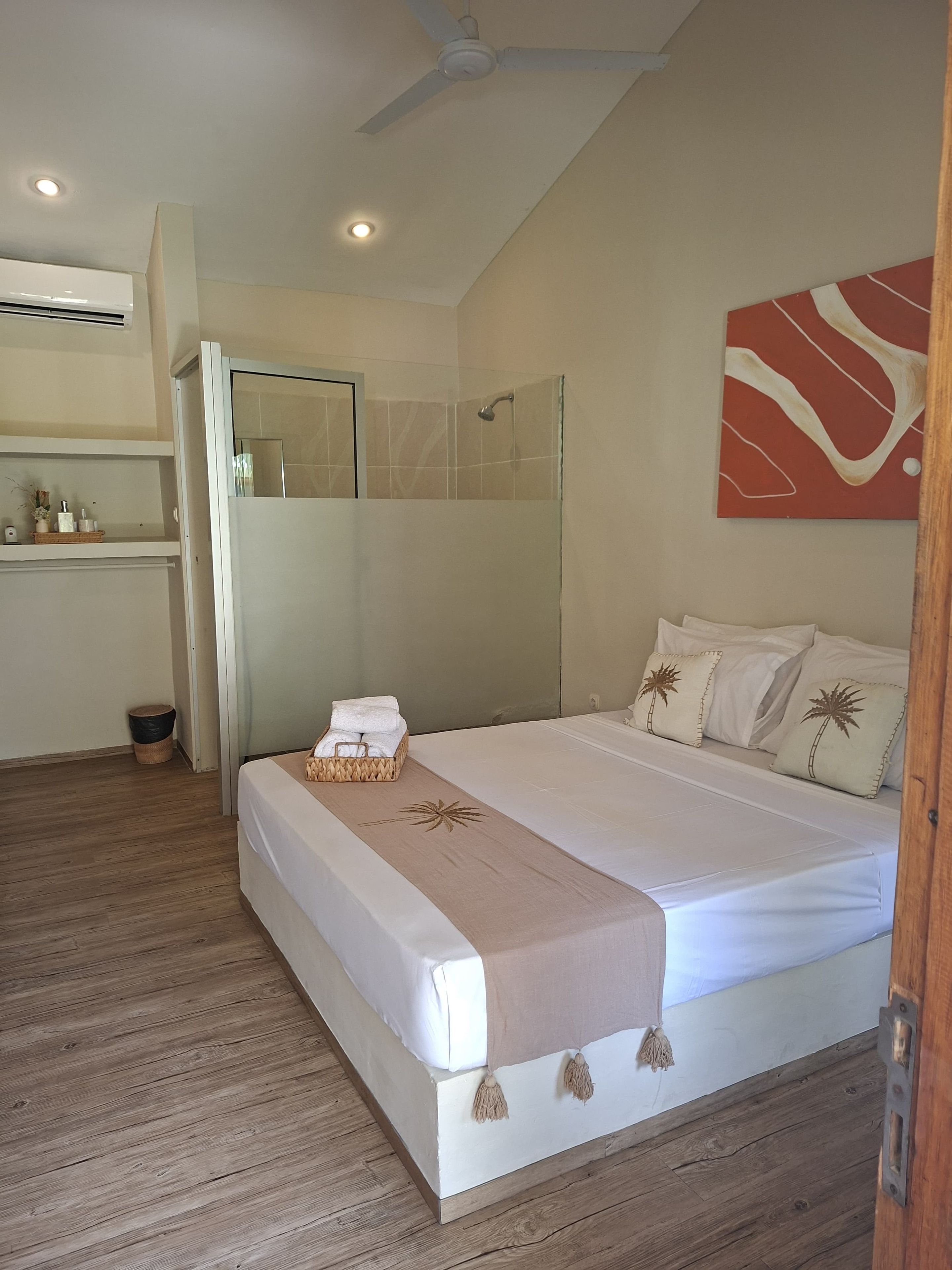 A hotel room with a bed, a shower, a ceiling fan, and a wall-mounted artwork.