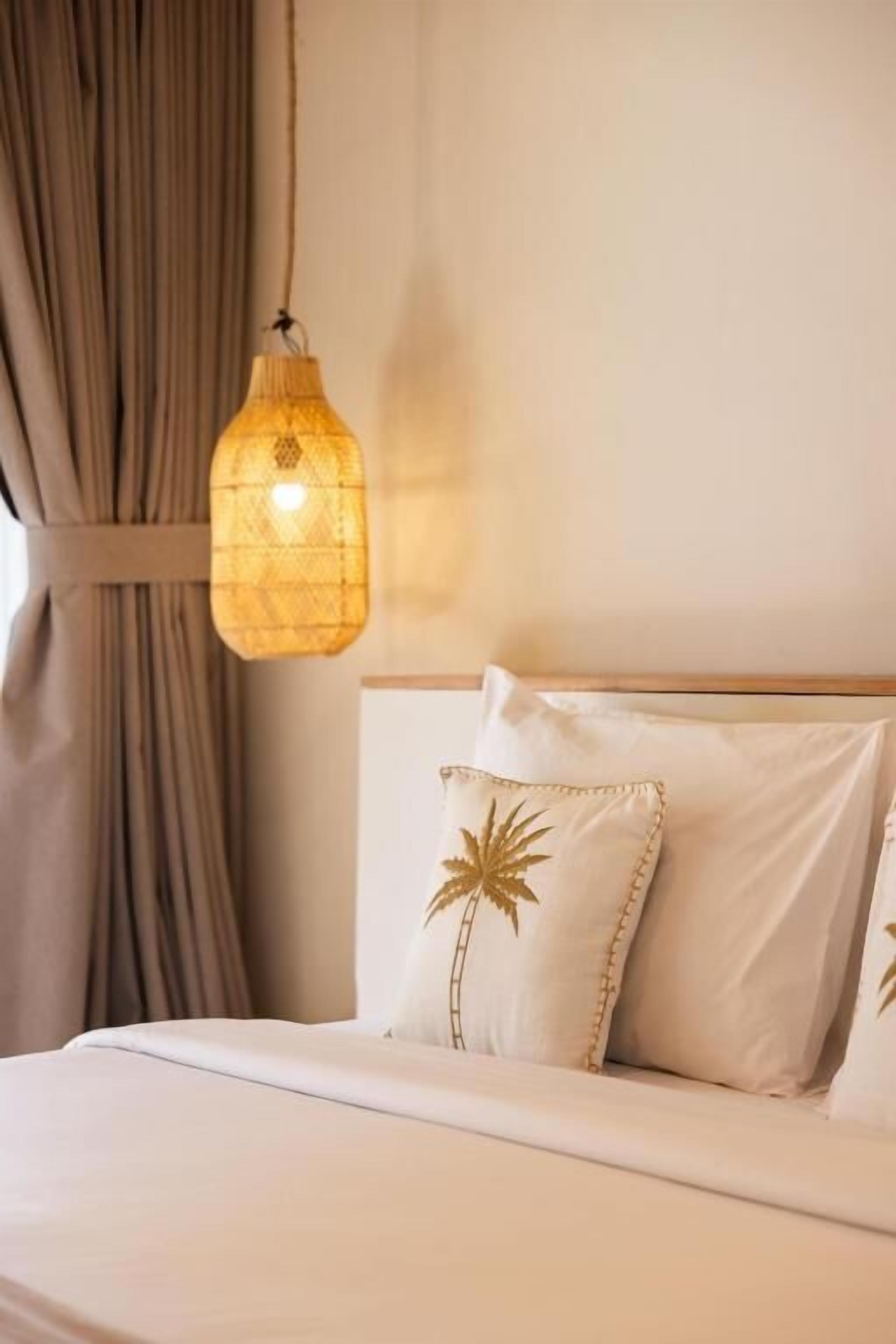Un lit avec une tête de lit, un luminaire suspendu et une fenêtre avec des rideaux.