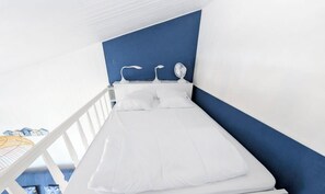 Una cama individual con ropa blanca en una habitación con paredes azules y blancas.