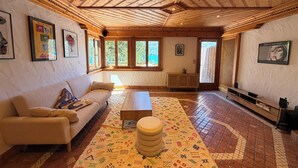 A spacious room with a wooden ceiling, a sofa, a coffee table, a patterned rug, and framed artwork on the walls. - Calimas House on the shores of Lake Annecy (Talloires-Montmin)