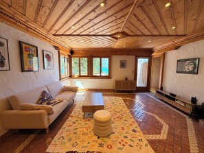 Ein geräumiger Raum mit Holzboden, einer Couch, einem Couchtisch, einem gemusterten Teppich und gerahmten Bildern an den Wänden.