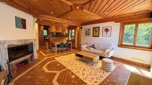 A spacious living area with a fireplace, a dining table, a sofa, and a kitchen in the background. - Calimas House on the shores of Lake Annecy (Talloires-Montmin)