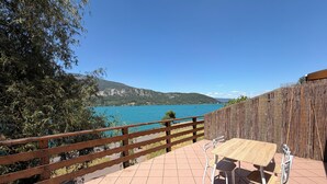 A patio with a table and chairs, overlooking a lake with a wooden fence and greenery. - Calimas House on the shores of Lake Annecy (Talloires-Montmin)
