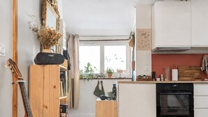 Une cuisine compacte avec des meubles blancs, un four encastré et une fenêtre agrémentée de plantes en pot.