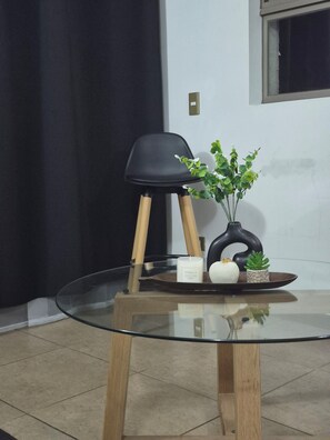 A glass-top table with a black chair, a potted plant, and a tray with candles and a vase. - Cozy Apartment with a Balcony, Pool, and Beautiful View in Valparaíso (Valparaíso)