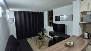 Ett kompakt kök med en matplats, en svart soffa och ett litet bord med en vattenkokare och en korg.