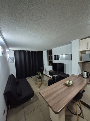 A compact kitchen with a dining area, a black sofa, and a small table with a kettle and a basket. - Cozy Apartment with a Balcony, Pool, and Beautiful View in Valparaíso (Valparaíso)