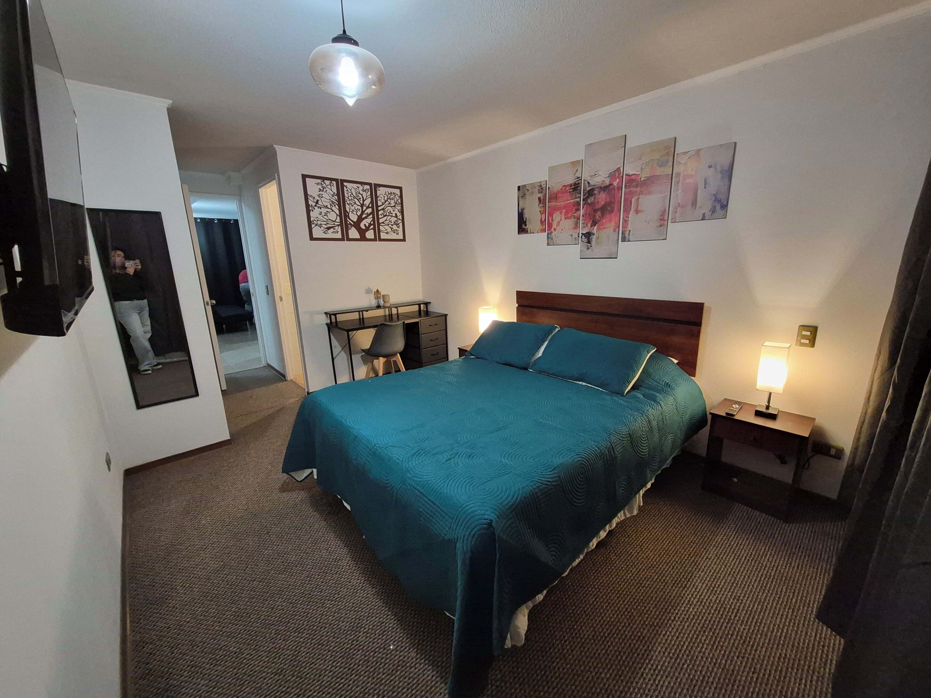 Une chambre d’hôtel équipée d’un lit, d’un bureau, d’une chaise, d’un miroir et d’œuvres d’art accrochées aux murs.